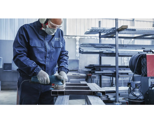 Ein Handwerker schleift ein Metallstück mit einer Schleifmaschine, während er Schutzkleidung trägt.