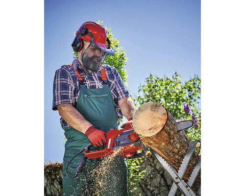 Mann sägt Holz mit einer elektrischen Kettensäge auf einem Sägebock im Freien, trägt dabei Schutzkleidung