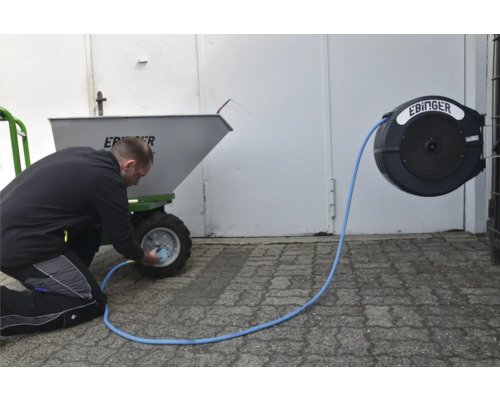 Eine Person füllt einen Reifen eines Dünge Streuwagens mit einem Druckluftschlauch auf, der an einer Schlauchtrommel befestigt ist.