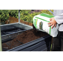 Ein Mann füllt Erde in ein Hochbeet im Gewächshaus.