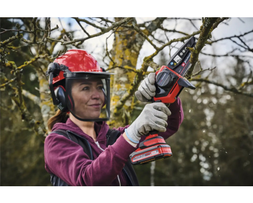 Frau mit Schutzhelm und Akku-Kettensäge beim Baumschnitt