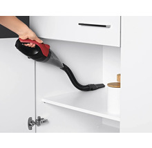 Eine Hand hält einen Handstaubsauger in einem weißen Schrank zur Reinigung.