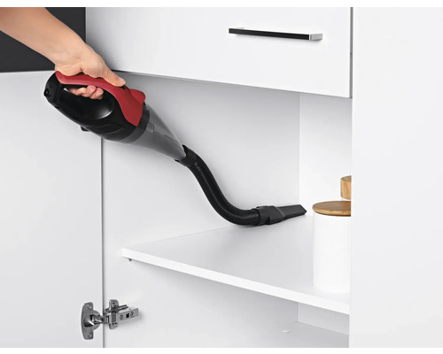 Eine Hand hält einen Handstaubsauger in einem weißen Schrank zur Reinigung.