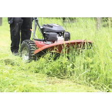 Person bedient eine rote Wildkrautbürste im hohen Gras.