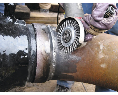 Eine Person reinigt eine Schweißnaht an einem Rohr mit einer Drahtbürste.