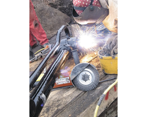 Rohrleitungsbau: Schweißer bei der Arbeit an einer Rohrverbindung mit Schweißausrüstung und Drahtbürste.