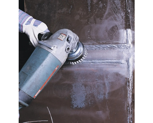 Eine Person benutzt eine Drahtbürste an einer Schleifmaschine zur Metallbearbeitung.