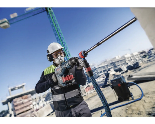 Ein Bauarbeiter mit persönlicher Schutzausrüstung verwendet einen Bohrhammer auf einer Baustelle.