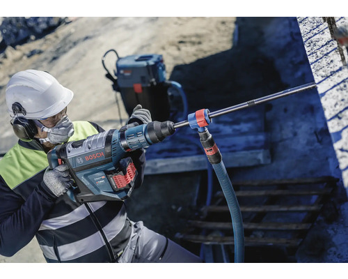 Mann mit Schutzhelm und Atemschutzmaske bedient einen Bohrhammer von Bosch auf einer Baustelle.