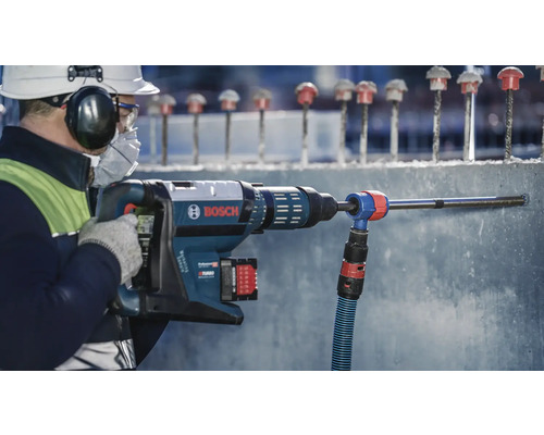 Ein Bauarbeiter bohrt mit einem Bohrhammer Löcher in eine Betonwand, wobei eine Staubabsaugung verwendet wird. Bosch Logo.