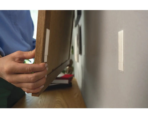 Eine Person befestigt mit Klebestreifen einen Bilderrahmen an der Wand.