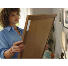 Frau befestigt Bild mit Klebestreifen an der Wand