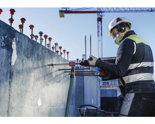 Ein Bauarbeiter bohrt mit einem Bohrhammer Löcher in eine Betonwand auf einer Baustelle
