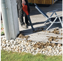Person benutzt einen Laubbläser auf einer Holzterrasse neben einem Liegestuhl.