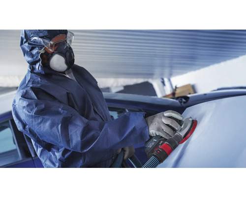 Person im Schutzanzug schleift ein Auto mit einem Schleifgerät.
