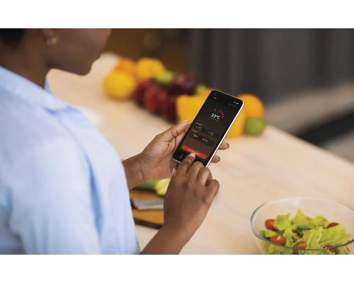 Frau bedient ein Smartphone mit Temperaturanzeige in der Küche