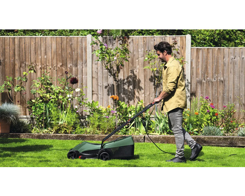 Ein Mann mäht den Rasen mit einem elektrischen Rasenmäher in einem Garten.