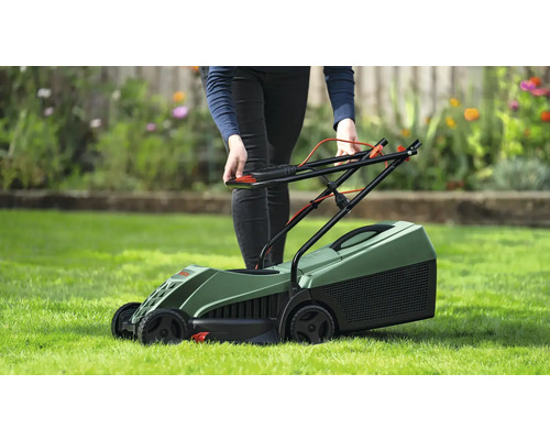 Eine Person bedient einen grünen Rasenmäher auf einer Rasenfläche.