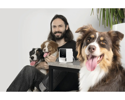 Mann sitzt mit drei Hunden und einer Haustierkamera an einem Tisch