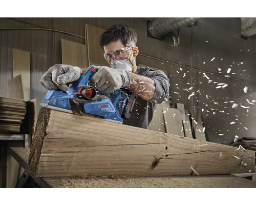 Mann hobelt Holzbrett mit einem Elektrohobel der Marke Bosch