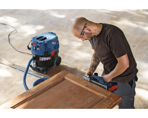 Handwerker hobelt Holztür mit einem Elektrohobel und einem Staubsauger