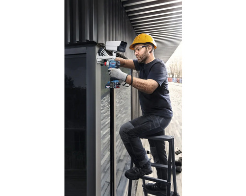 Ein Handwerker montiert mit einem Akku-Bohrschrauber eine Überwachungskamera auf einer Leiter.