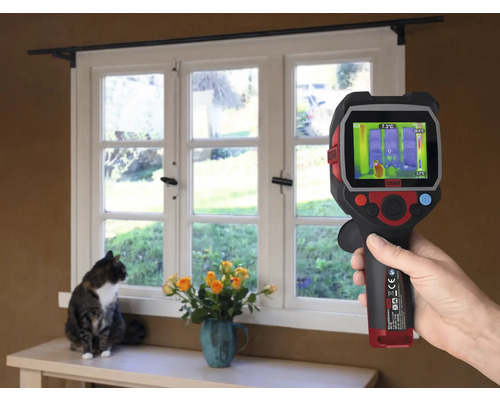 Eine Hand hält eine Wärmebildkamera vor ein Fenster, während eine Katze auf der Fensterbank sitzt.