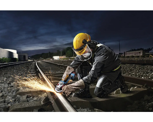 Ein Arbeiter schleift eine Eisenbahnschiene mit einem Winkelschleifer und erzeugt dabei Funken.