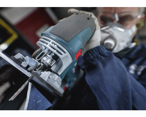 Eine Stichsäge im Einsatz beim Sägen von Material, bedient von einer Person mit Schutzmaske und Schutzbrille.