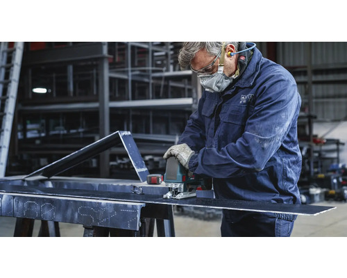 Ein Handwerker schneidet mit einer Stichsäge ein Metallstück. Er trägt Schutzkleidung.