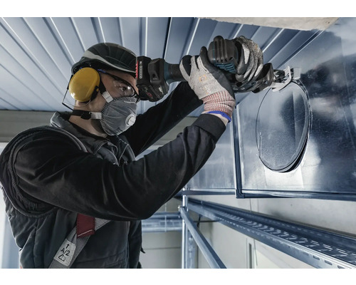 Eine Person schneidet mit einer Blechschere ein Loch in ein Lüftungsrohr.