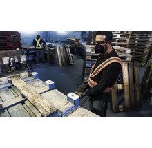 Arbeiter repariert mit Werkzeug in einer Werkstatt Holzpaletten.