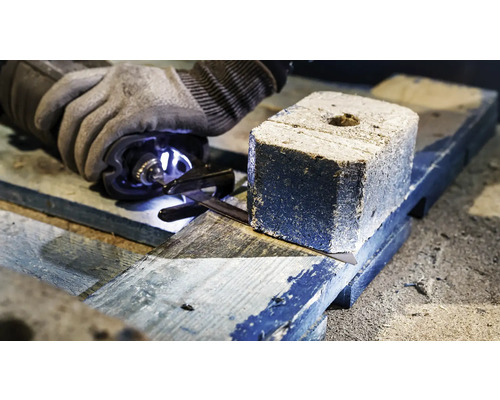 Eine Person sägt eine Holzkohlebrikett auf einem Holzbrett mit einer Säge.