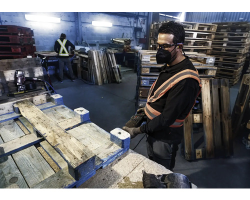 Ein Arbeiter repariert eine Palette mit einem Druckluftnagler in einer Werkshalle.