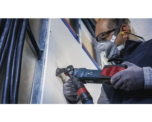 Handwerker schneidet mit einem Multifunktionswerkzeug eine Öffnung in eine Gipskartonwand.