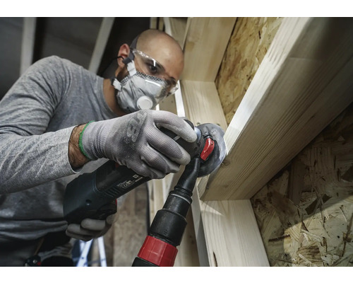 Handwerker bearbeitet Holz mit einem Multifunktionswerkzeug, inklusive Staubabsaugung, Schutzbrille und Atemschutz.