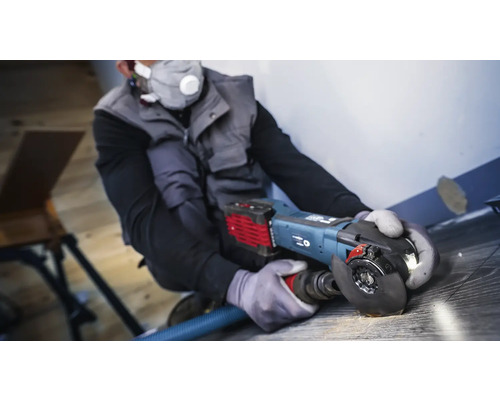 Handwerker verwendet einen Winkelschleifer mit Staubabsaugung auf einem Holzboden