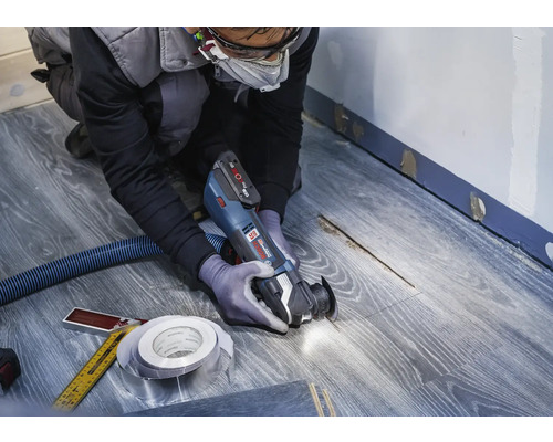 Handwerker verwendet Multifunktionswerkzeug auf Laminatboden für Renovierungsarbeiten.