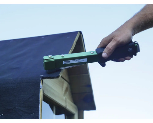 Handwerker befestigt Dachpappe mit einem Handtacker auf einem Holzhaus.