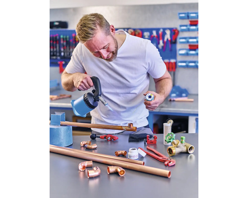 Mann lötet Kupferrohre mit Lötlampe und Lötzinn in einer Werkstatt.