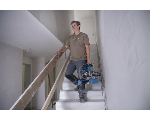 Handwerker trägt eine Paneelsäge eine Treppe hinunter in einem Haus im Bau.