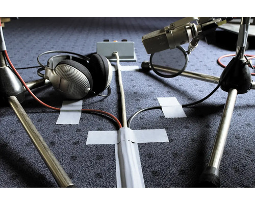 Szene mit zwei Mikrofonen, Kopfhörern und Kabeln, die mit Klebeband auf dem Boden befestigt sind.
