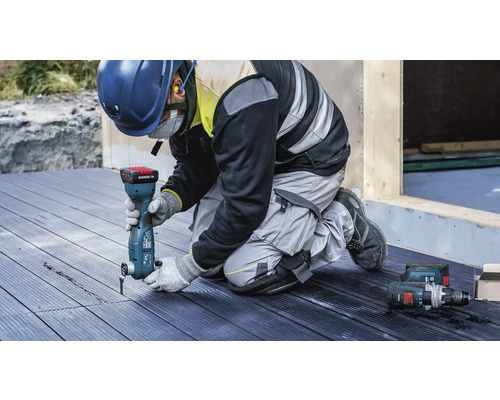 Ein Arbeiter verwendet ein Multifunktionswerkzeug auf einer Holzterrasse. Persönliche Schutzausrüstung ist ebenfalls vorhanden.