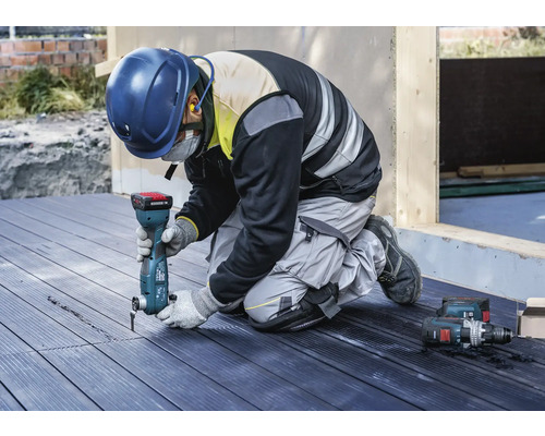 Handwerker kniet auf einer Terrasse und arbeitet mit einem Multifunktionswerkzeug