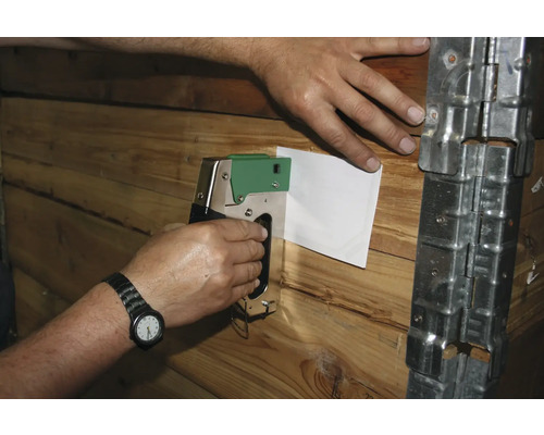 Eine Person befestigt ein Blatt Papier mit einem Tacker an einer Holzwand.