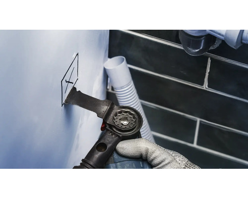 Handwerker schneidet mit einem Multifunktionswerkzeug ein Loch in eine Wand