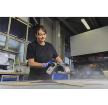 Frau sprüht Farbe auf ein Werkstück mit einer Sprühdose.