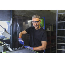 Mann mit Schutzbrille und Handschuhen, der an einer Werkbank arbeitet.