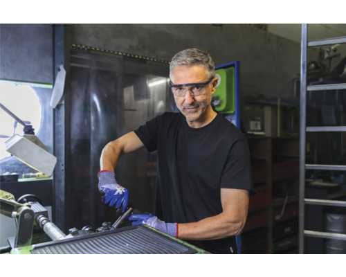 Mann mit Schutzbrille und Handschuhen, der an einer Werkbank arbeitet.