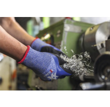 Hände mit Schutzhandschuhen halten Metallspäne vor einer Drehmaschine